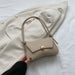 Beige handbag held by a hand against a white background