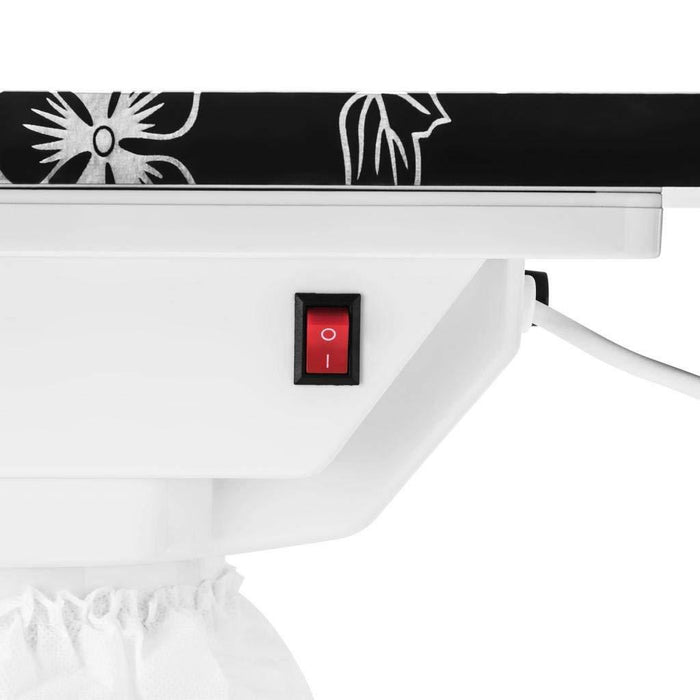 Close-up of a white iron with a black and white floral design on the top, featuring a red power switch.
