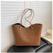 A brown leopard-print tote bag with two long shoulder straps and gold-tone hardware, resting on a black leather sofa in front of white paneled walls.