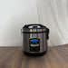Stainless steel rice cooker on a wooden surface with a white curtain background