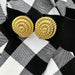Gold textured earrings on a black and white checkered background