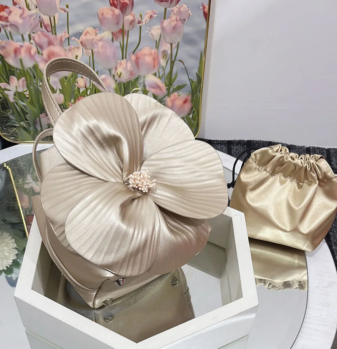 Beige floral handbag and matching pouch on a white surface with flowers in the background