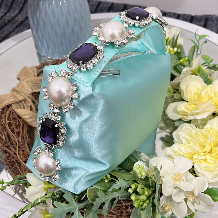 Turquoise handbag with decorative pearls and gemstones on a floral background