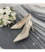 Pair of lace high-heeled shoes next to a bouquet of white roses on a gray surface.