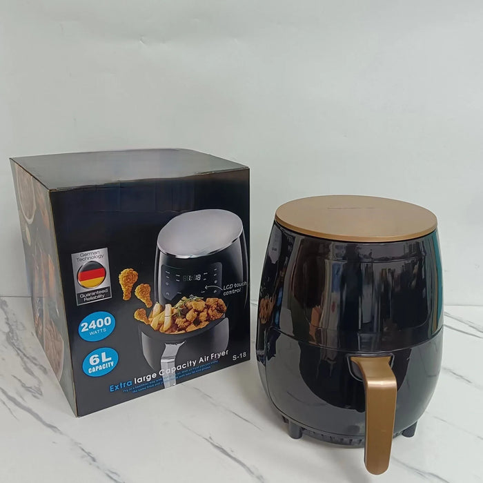 Black air fryer with gold handle next to its packaging on a white surface