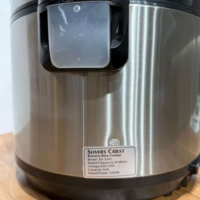 Silver electric rice cooker with a visible brand label on a wooden surface.