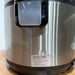 Silver electric rice cooker with a visible brand label on a wooden surface.