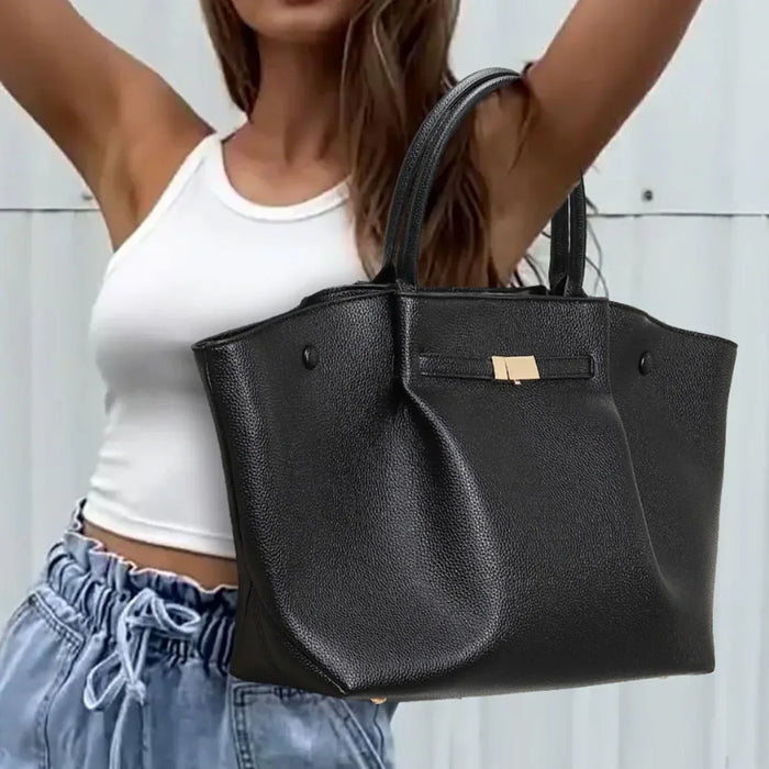 Person holding a black leather handbag against a neutral background