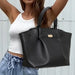 Person holding a black leather handbag against a neutral background