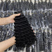 Person holding a bundle of black hair extensions with a background of more hair extensions in packaging.