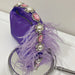 Purple handbag with decorative elements including pearls and feathers on a white surface.