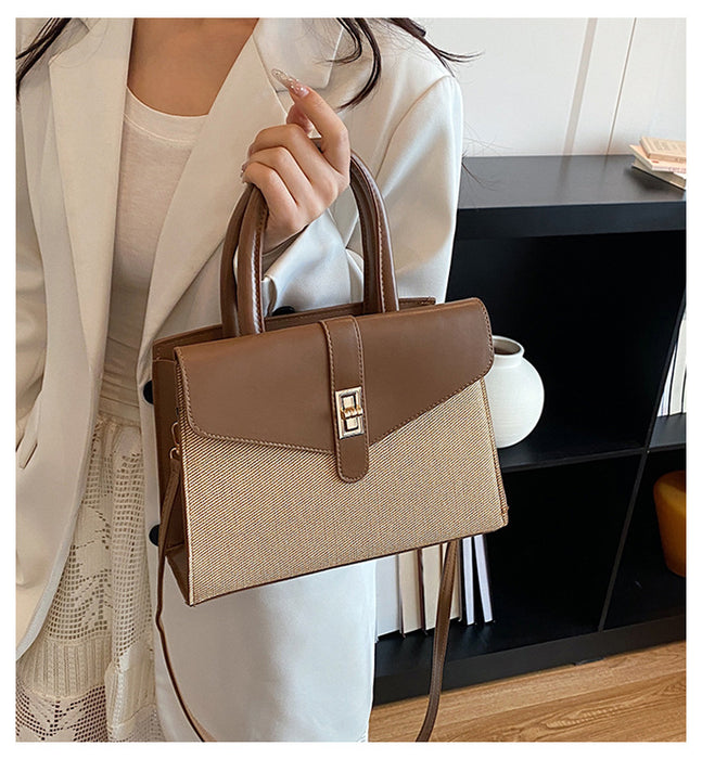 A woman in a white blazer holds a structured handbag with a woven beige body, brown leather trim and handles, and a gold-tone front clasp. The setting appears to be an indoor room with a dark shelf in the background.