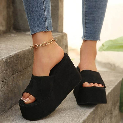 Black platform sandals worn with blue jeans on a stone step.
