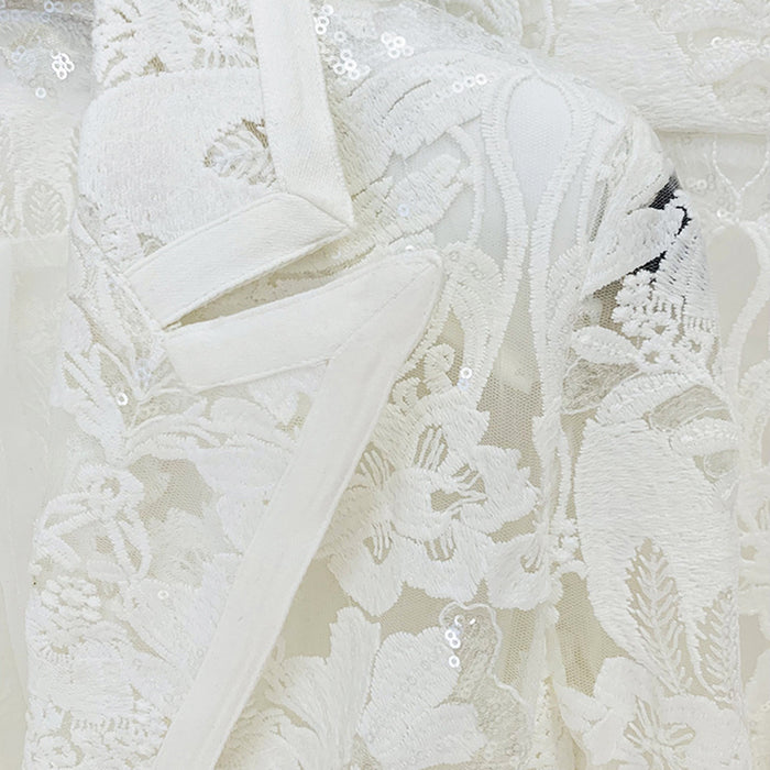 Close-up of intricate lace fabric with sequins on a light background