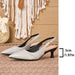 A pair of pointed-toe slingback pumps in a light metallic champagne-gray textured material with black heels and straps, displayed on a woven mat with a boho wall hanging in the background. A size marker indicating 5cm / 1.