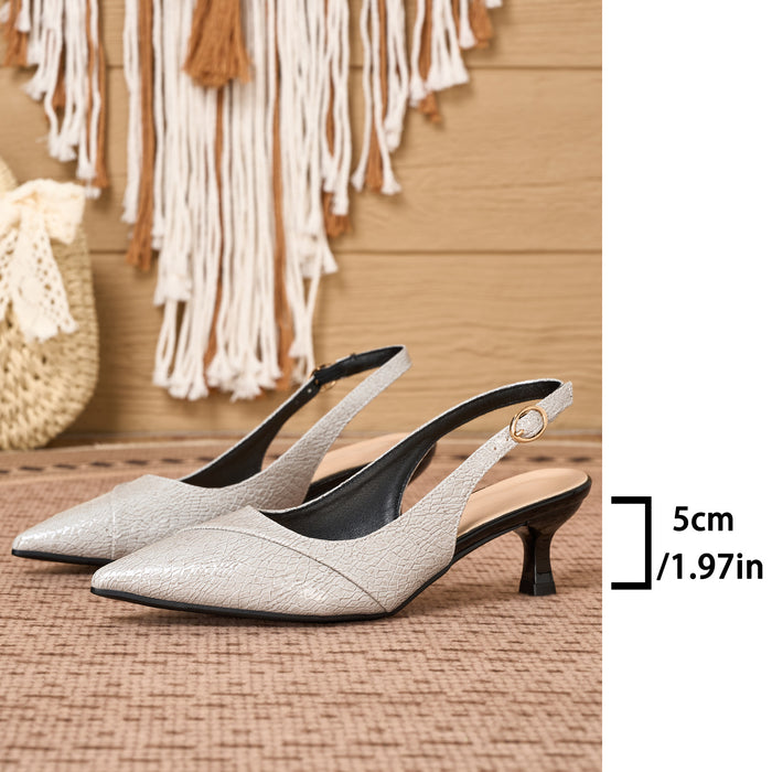 A pair of pointed-toe slingback pumps in a light metallic champagne-gray textured material with black heels and straps, displayed on a woven mat with a boho wall hanging in the background. A size marker indicating 5cm / 1.