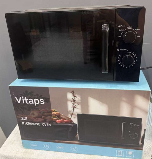 A black Vitaps 20L microwave oven sits on top of its blue and white retail box. The microwave has a glossy black finish with a silver handle and control knobs on the right side.