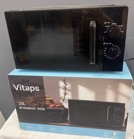A black Vitaps 20L microwave oven sits on top of its blue and white retail box. The microwave has a glossy black finish with a silver handle and control knobs on the right side.