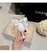 White decorative item with a bow in a Chanel box on a light surface.