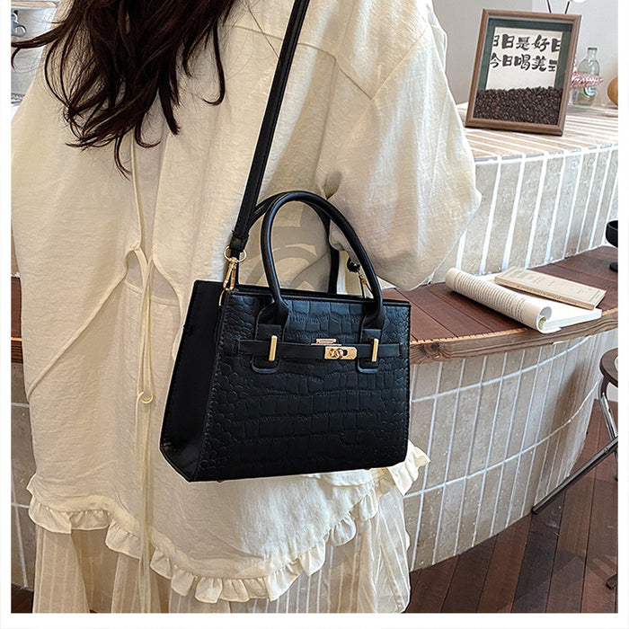 A woman wearing a cream-colored ruffled blouse carries a structured black crocodile-embossed handbag with gold-tone hardware and a shoulder strap in an indoor setting.