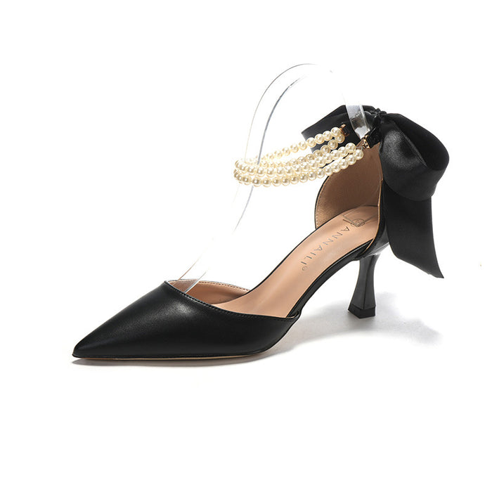 Black high-heeled shoe with a bow and pearl detail on a white background