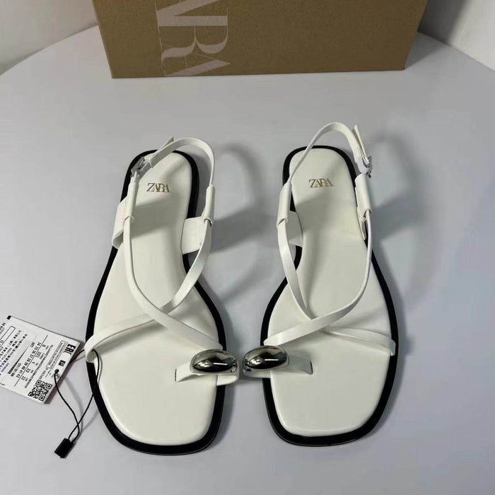 White sandals with a bow detail on a light gray surface, with a Zara box in the background.