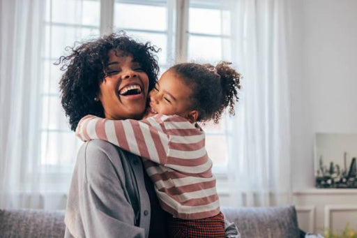 Woman and child hugging in a bright room with large windows.