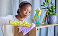 Woman cleaning a table with a plant and cleaning supplies in the background