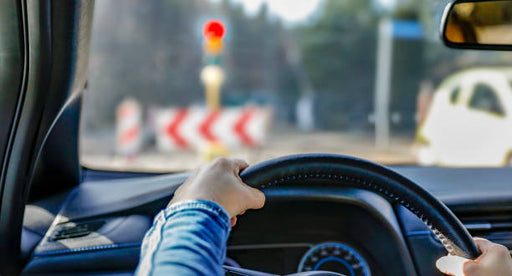 Person driving a car with traffic lights and road signs visible through the windshield.