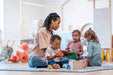 Woman playing with children on a rug in a room with toys.