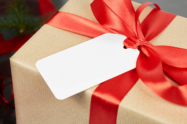 Gift wrapped in brown paper with a red ribbon and white tag on a blurred background